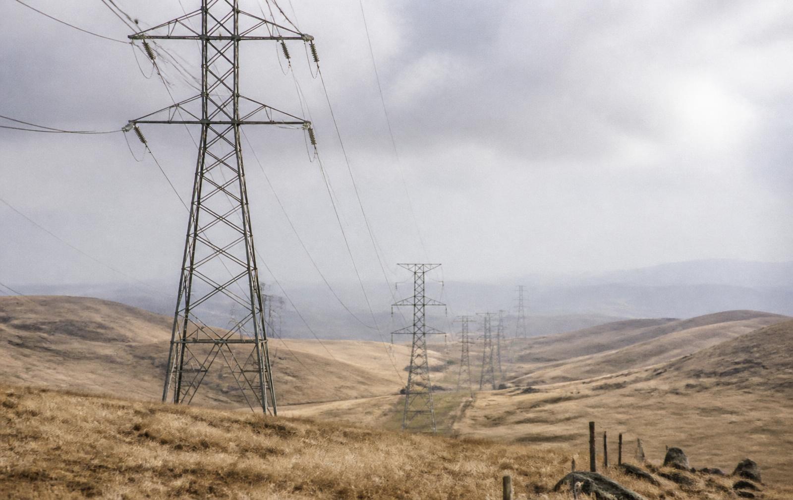 Transmission towers crossing dry grassland hills under an overcast sky